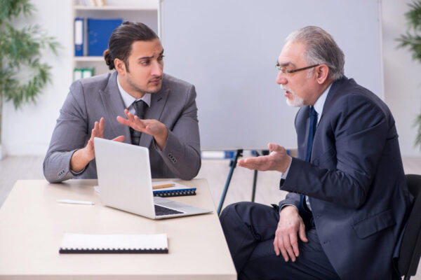 Abbildung: 2 Mitarbeiter diskutieren zusammen am Tisch vor dem laptop