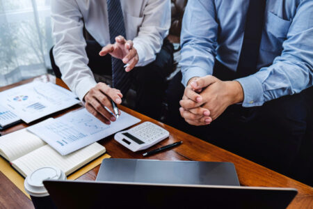 Abbildung: Hände mit Tisch voller Bilanzen zeigen auf einen Laptop